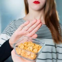 A bowl of peanuts is offered to a young woman who holds up her hand to say no. 
